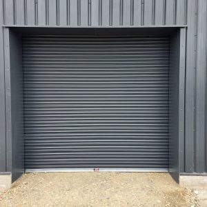 Anthracite grey industrial roller shutter door fitted to the exterior of a modern steel-clad commercial building.