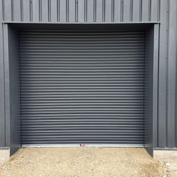 Anthracite grey industrial roller shutter door fitted to the exterior of a modern steel-clad commercial building.