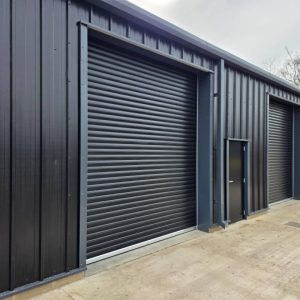 Close up of a black galvanized steel roller shutter door and matching personnel security door on a commercial unit.