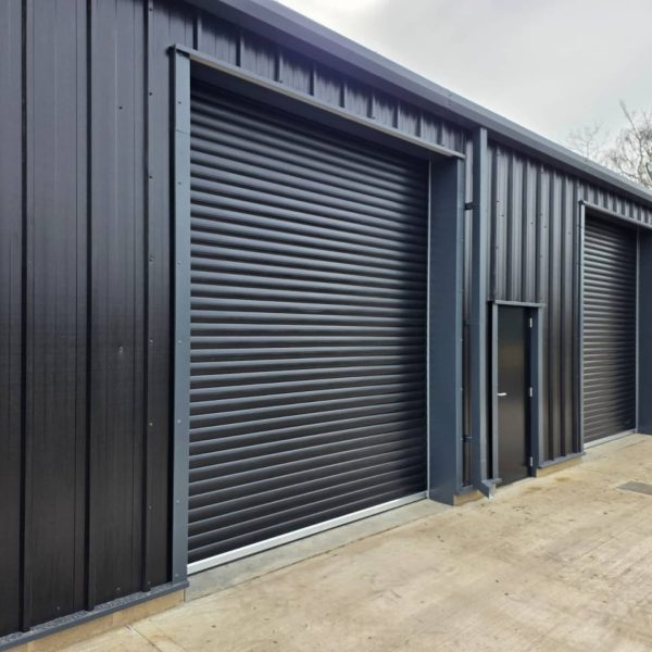 Close up of a black galvanized steel roller shutter door and matching personnel security door on a commercial unit.