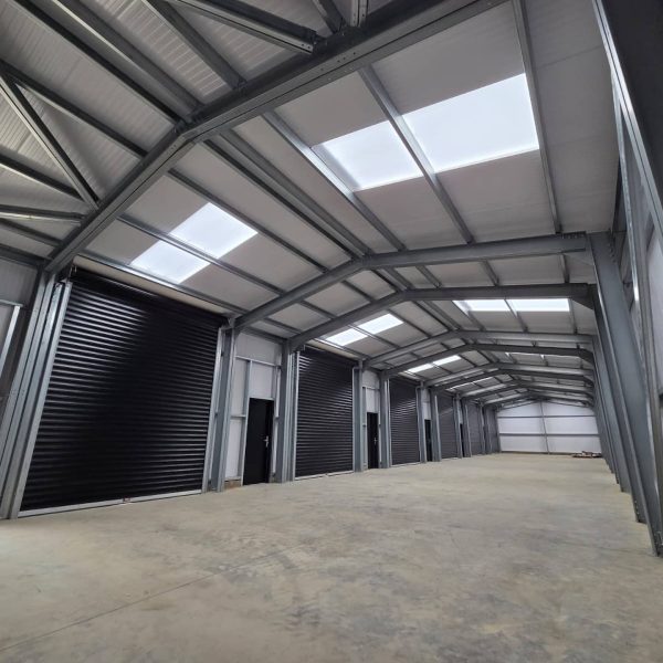Interior view of a large steel-framed agricultural or industrial building featuring a row of black commercial roller shutter doors.