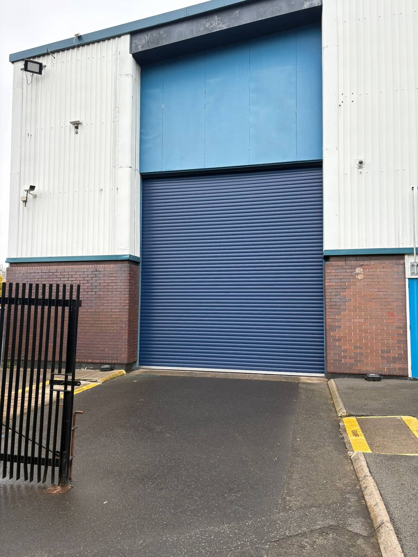 Large blue commercial steel roller shutter door fitted to the exterior loading bay of an industrial warehouse.