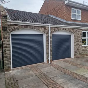 Twin Anthracite Grey insulated residential roller garage doors custom-fitted beneath arched brickwork on a stone-built home.