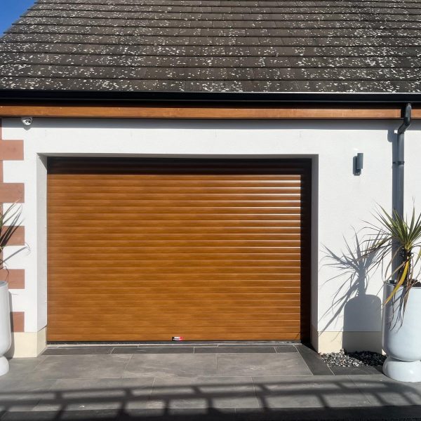 Golden oak woodgrain finish insulated residential roller garage door fitted to a modern white rendered home.