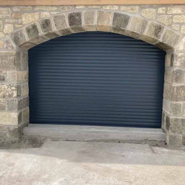 Anthracite grey insulated residential roller garage door installed seamlessly behind a traditional rustic stone archway.