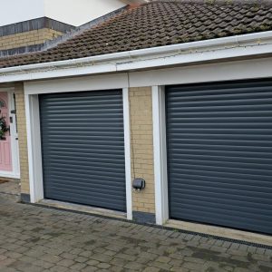 Two side-by-side Anthracite Grey insulated residential roller garage doors with contrasting white guide rails fitted to a brick home.