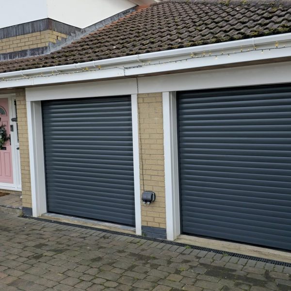 Two side-by-side Anthracite Grey insulated residential roller garage doors with contrasting white guide rails fitted to a brick home.