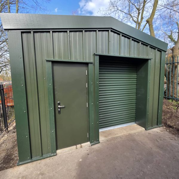 Green commercial steel roller shutter door and matching personnel access door fitted to a secure outdoor metal storage building.