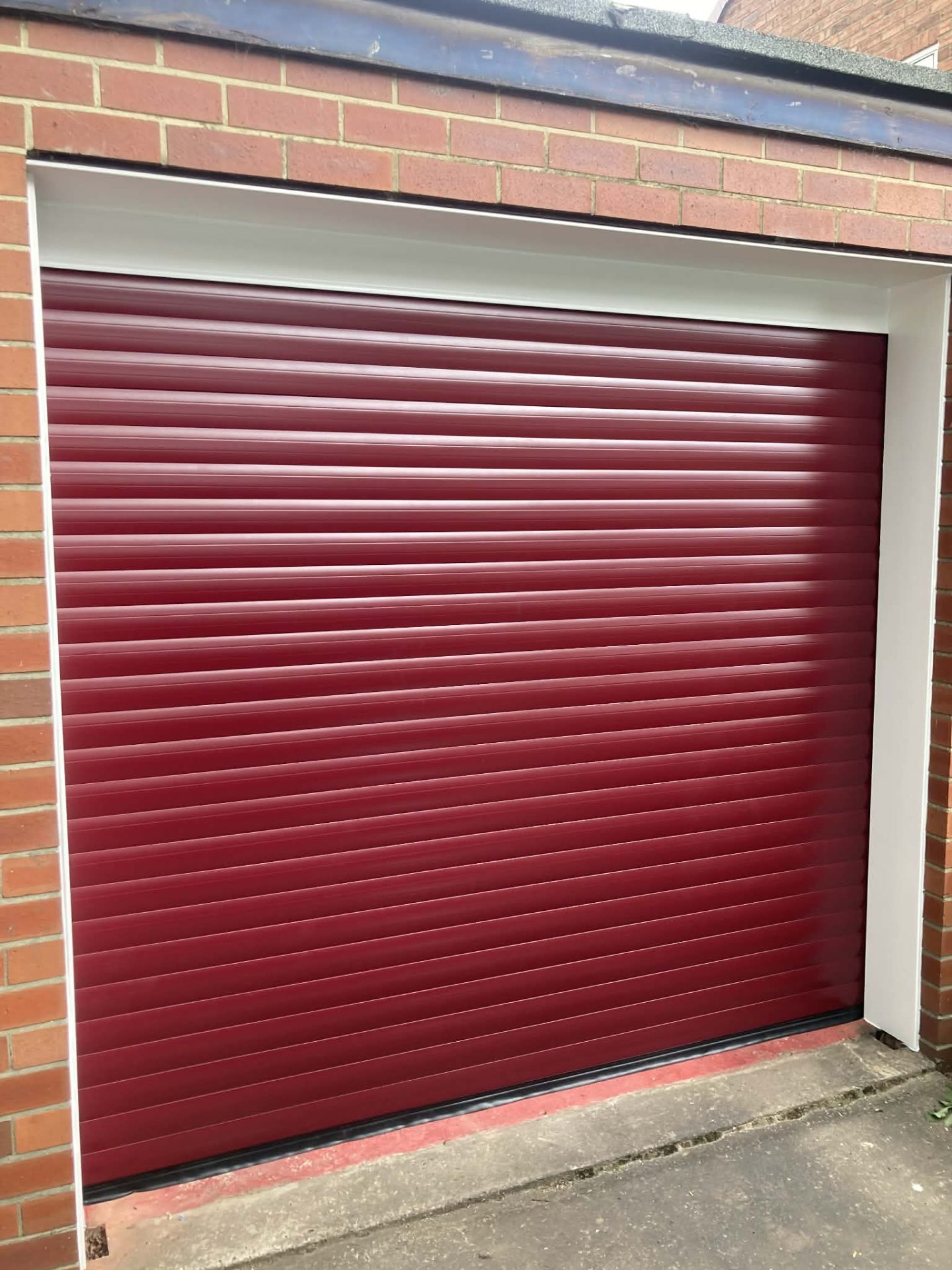 Burgundy red roller garage door on a sandstone cottage