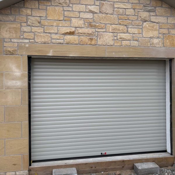 Light grey insulated residential roller garage door installed in a newly built stone garage under construction.