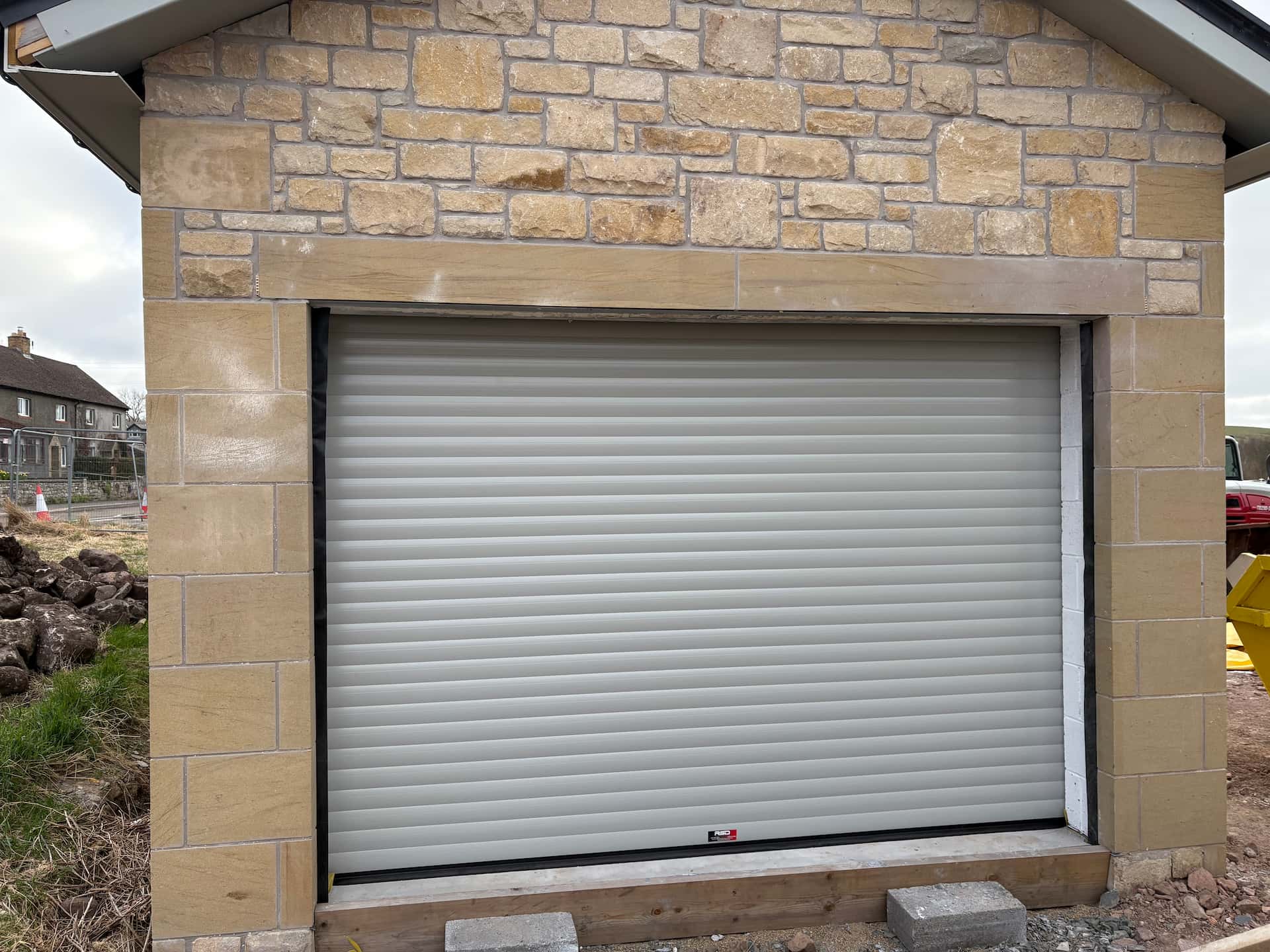 Light grey insulated residential roller garage door installed in a newly built stone garage under construction.