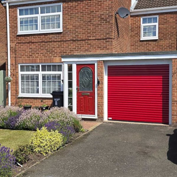 Bright red insulated residential roller garage door with white guide rails, color-matched to the front door of a brick terraced home.